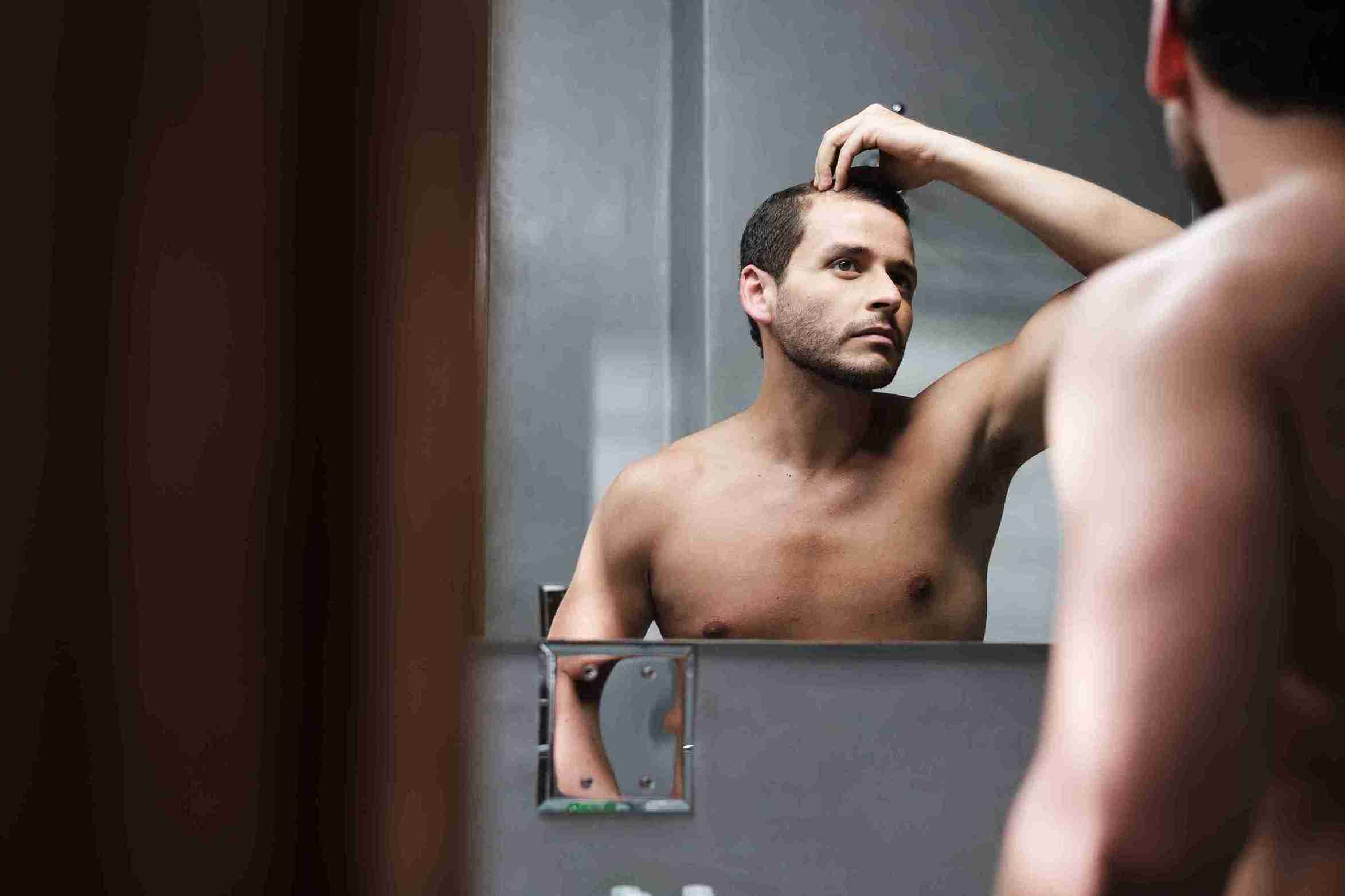 Mann schaut in den Spiegel seine Haare an und denke über mögliche Haartransplantation Risiken nach.