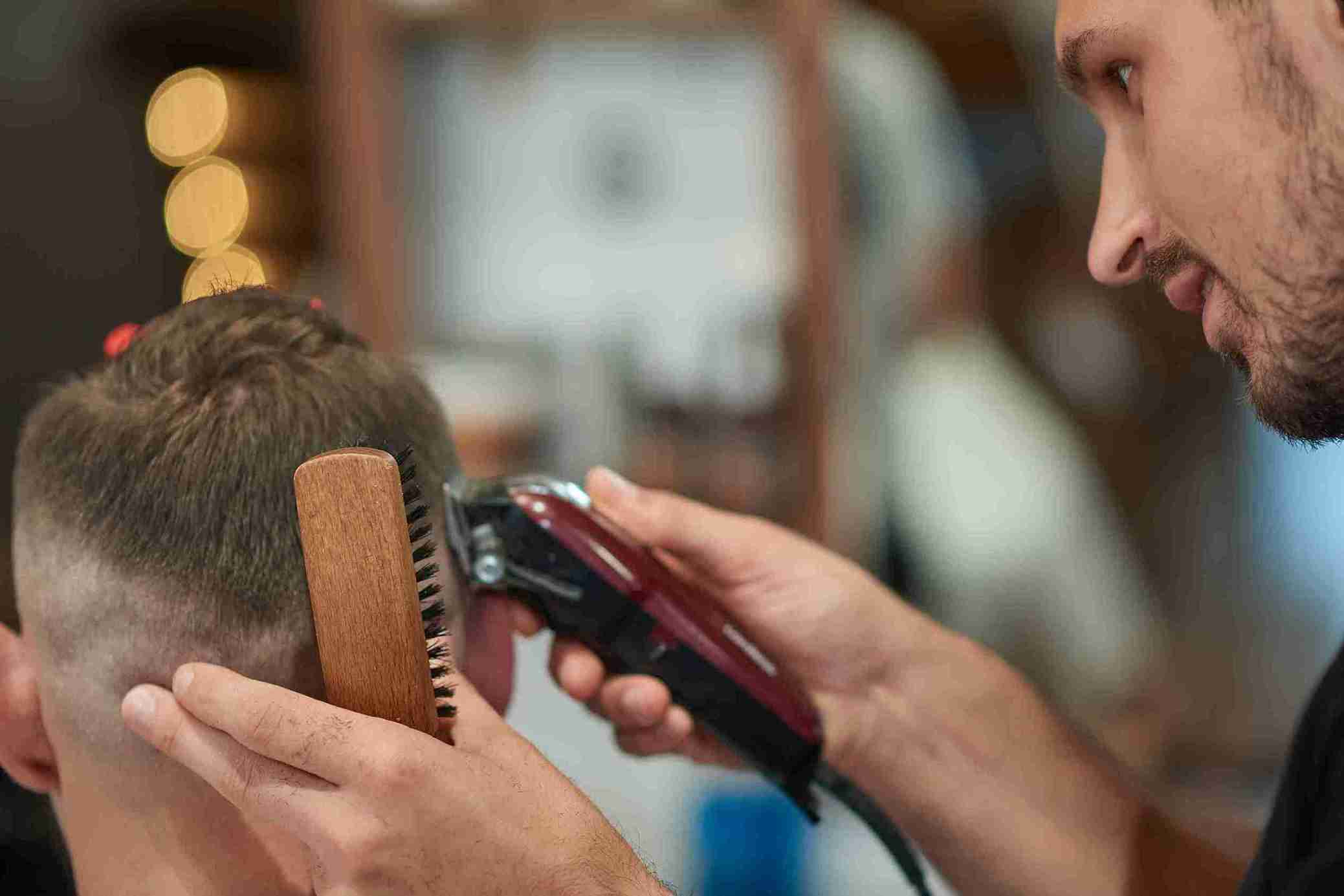 Friseur schneidet einem Mann vorsichtig die Haare mit Maschine und Bürste – Haare schneiden nach Haartransplantation Schritt für Schritt.