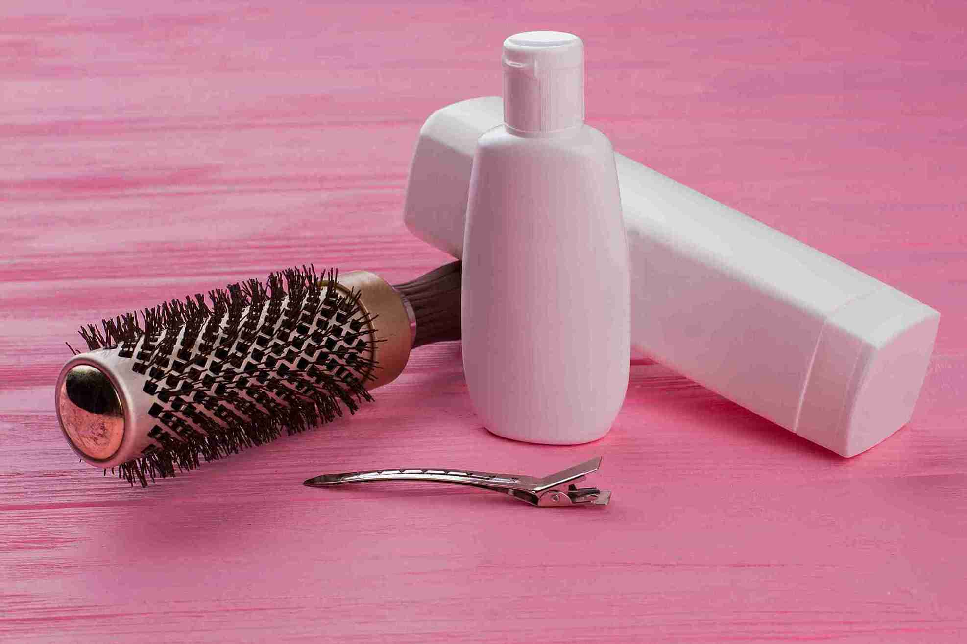 Pflege nach Haartransplantation mit Haarbürste, Haarspange und Pflegeprodukten auf rosa Hintergrund.