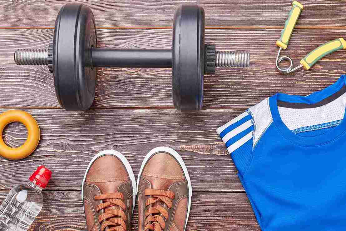 Sport nach Haartransplantation – ab wann wieder trainieren? Auf dem Bild liegen Hantel, Sportshirt, Schuhe, Wasserflasche und Zubehör bereit.