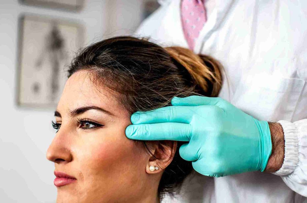 Close-up of a doctor in gloves examining a female patient's hairline during a consultation for Women Hair Transplant Turkey.