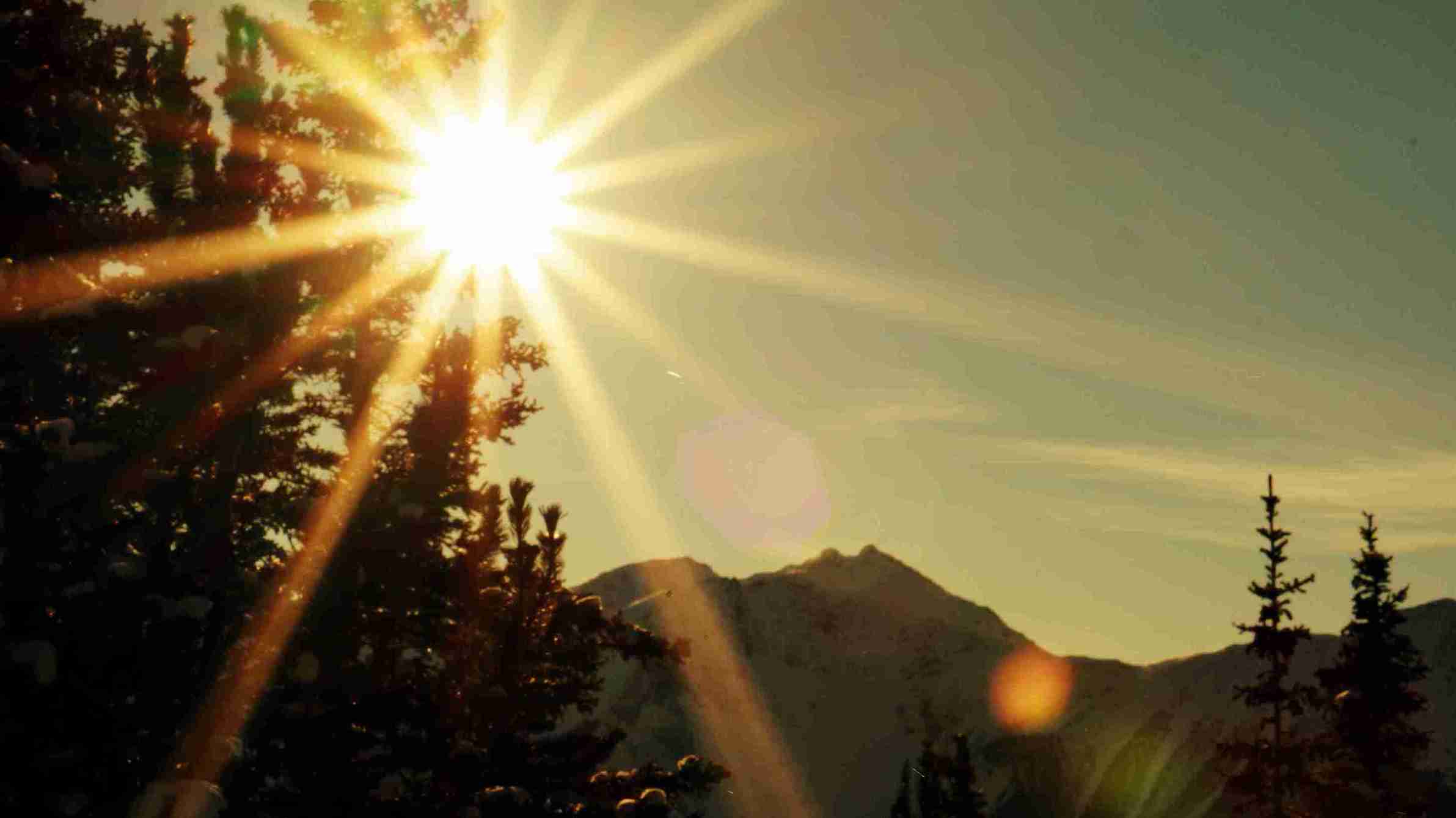 Bright sun shining over mountain landscape with trees, representing recovery and sun protection – How Long to Avoid Sun After Hair Transplant.