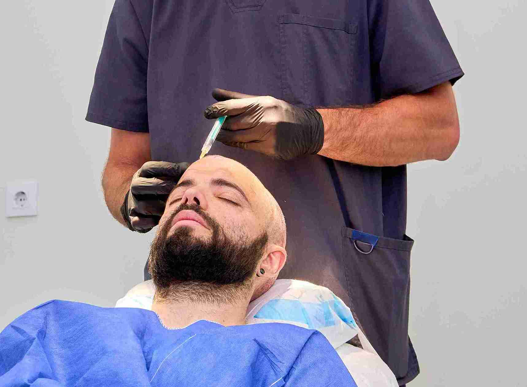 A patient lies in a medical chair while a clinician wearing gloves injects solution into his scalp during a hair transplant procedure, illustrating how does a hair transplant work in a clinical setting.